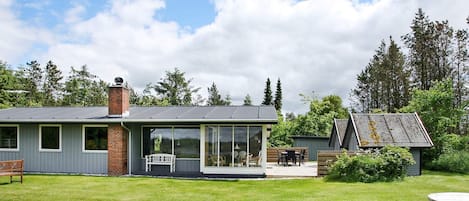 A modern house with a large glass extension, a deck, and a small shed in a grassy yard.