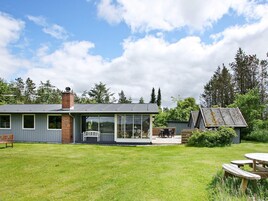 A modern house with a large glass extension, a deck, and a small shed in a grassy yard.