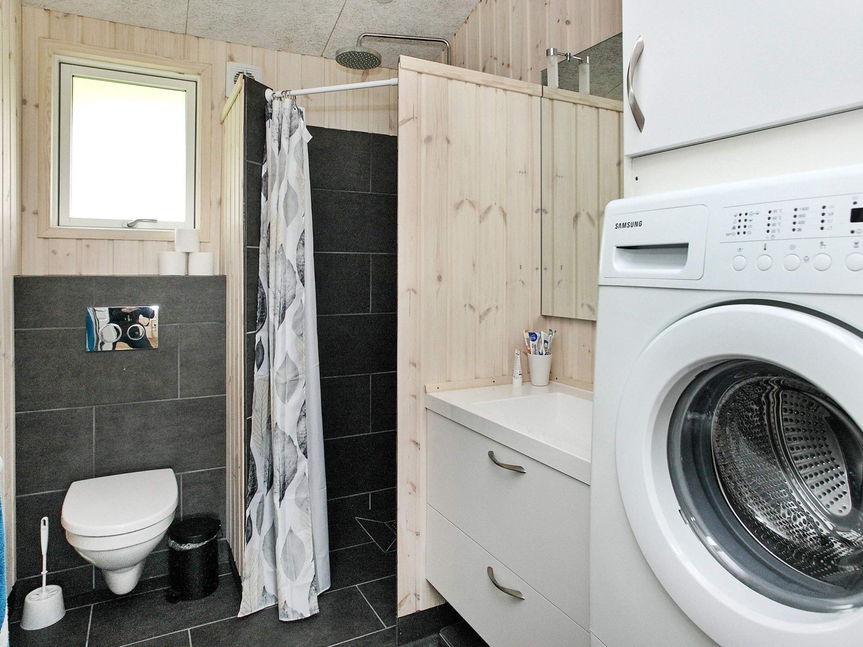 A compact bathroom with a toilet, shower, and washing machine.