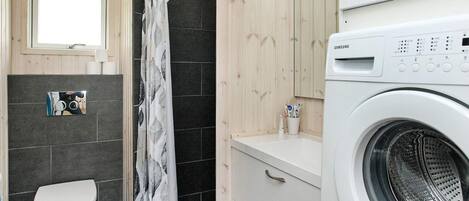 A compact bathroom with a toilet, shower, and washing machine.
