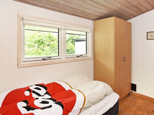 A bedroom with a bed, a window, and a wooden wardrobe.