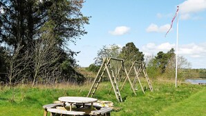 A picnic area with a wooden table and benches, surrounded by trees and a flagpole. - Spacious Holiday Home in Højslev near Sea (Hojslev)