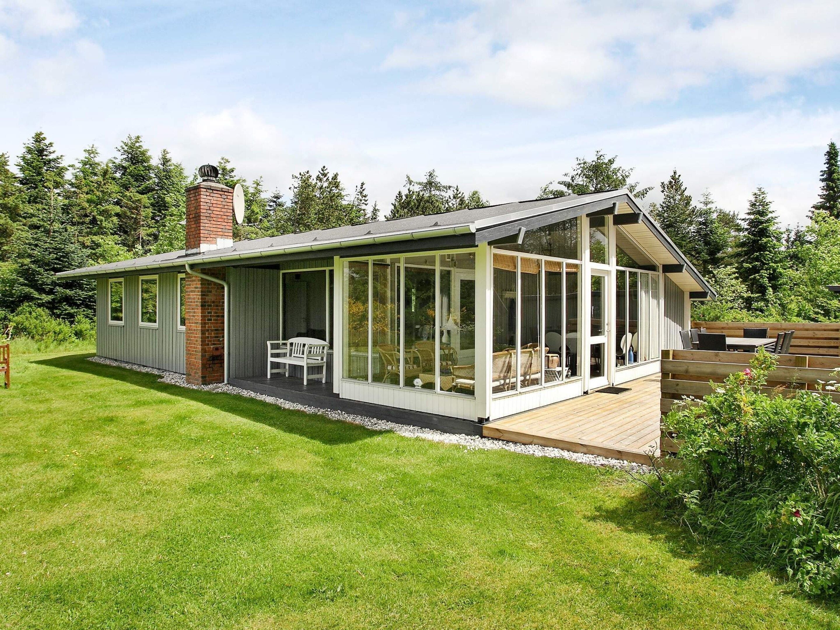 A single-story house with a covered patio, a brick chimney, and a deck with outdoor furniture.