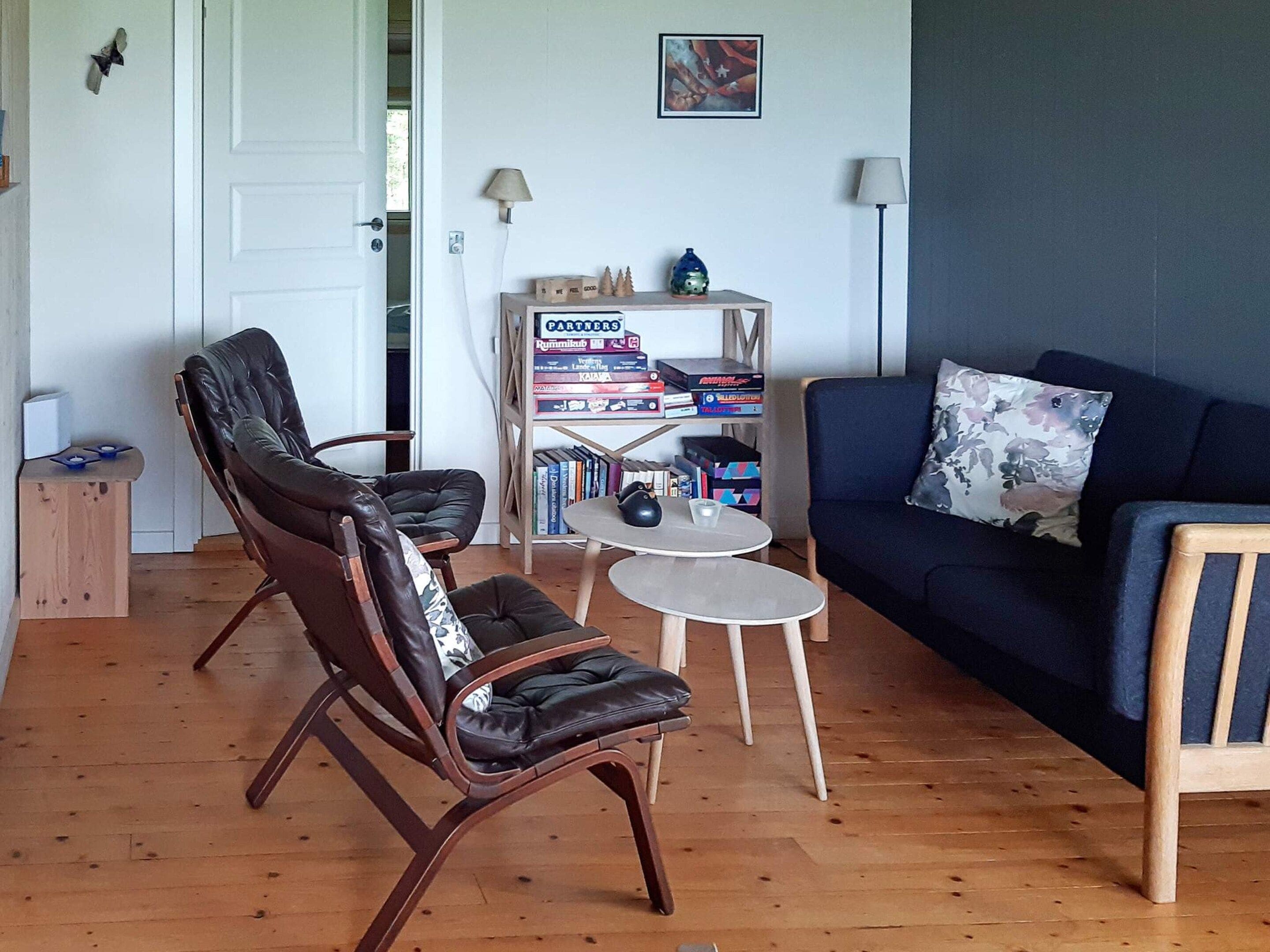 A living room with a dark blue sofa, two leather chairs, a small round table, and a bookshelf with various items.