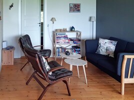 A living room with a dark blue sofa, two leather chairs, a small round table, and a bookshelf with various items.