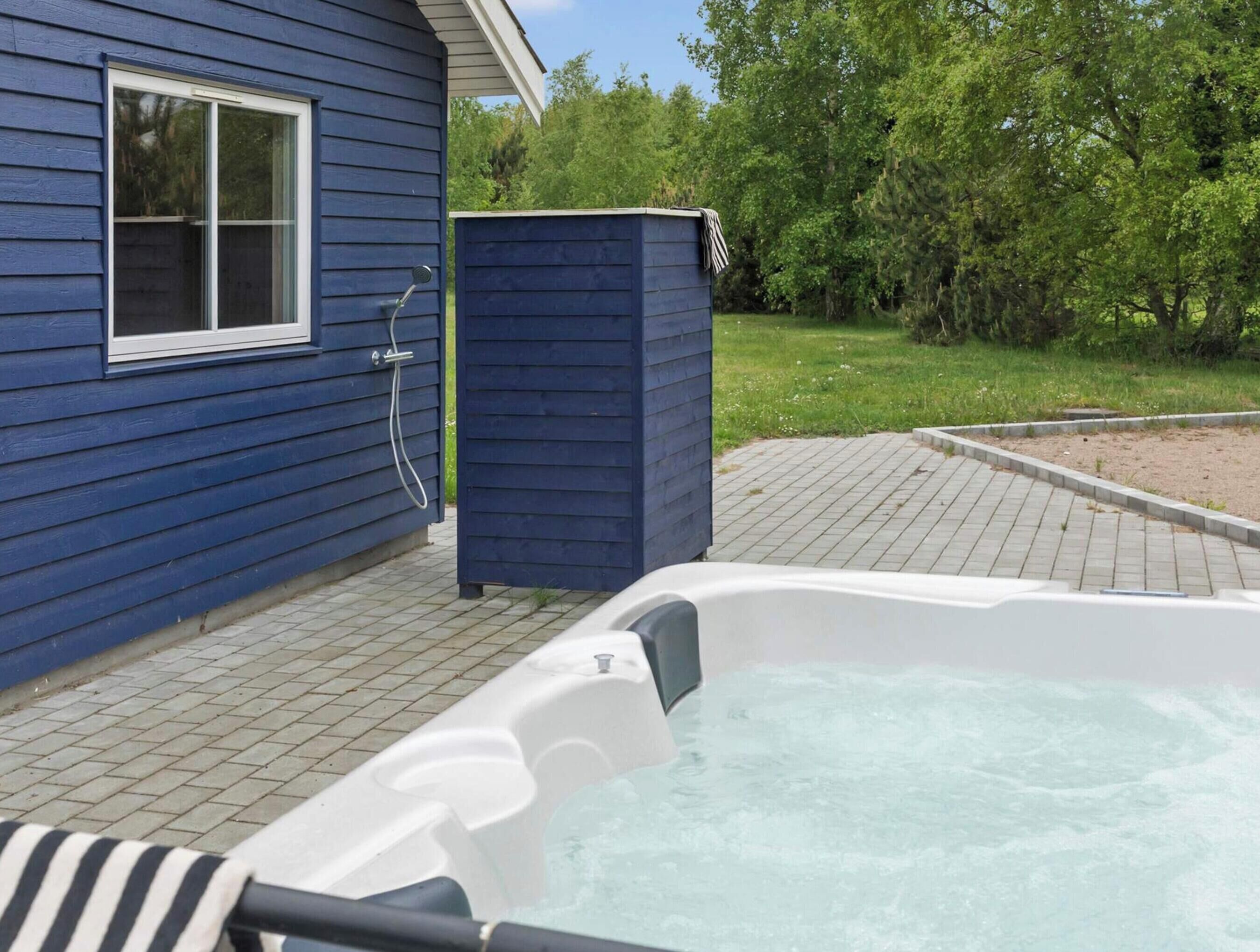 A hot tub in a backyard with a blue house and a wooden deck.