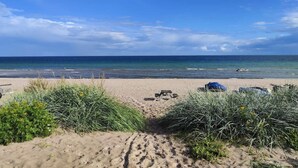 Een strand met zand, zee en schaarse begroeiing.