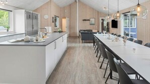 Een moderne keuken met een centraal eiland, houten paneelwanden en een eethoek met een lange tafel en stoelen.