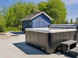 A hot tub with a wooden exterior, a small shed, and a paved patio area. - 5 Star Holiday Home in Vaeggerlose (Vaeggerlose)