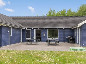 A blue building with a tiled roof, a patio with a table and chairs, and a grill area. - 5 Star Holiday Home in Vaeggerlose (Vaeggerlose)