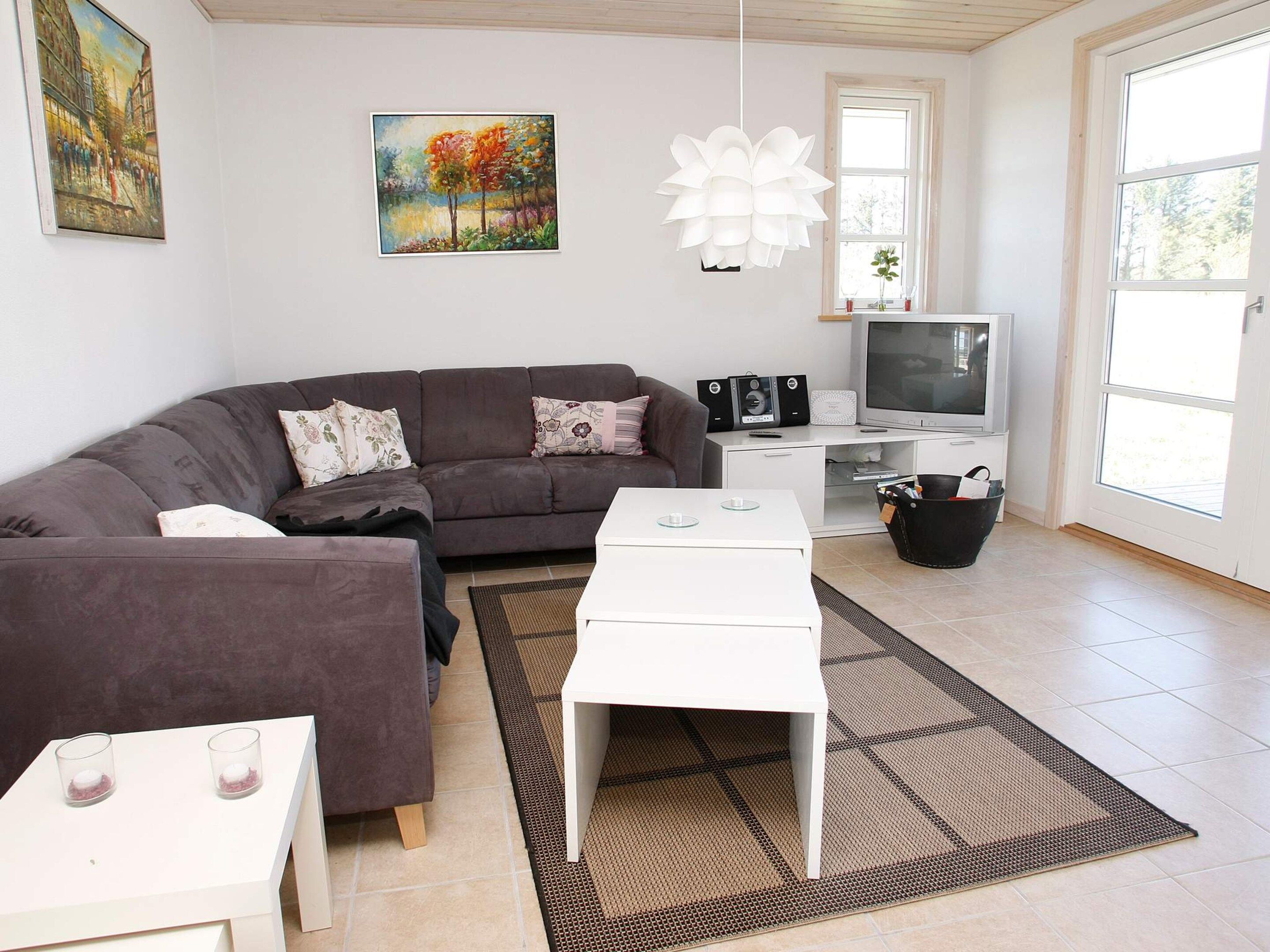 Un salon moderne avec un canapé, une table basse et un téléviseur. Un tableau orne le mur et une fenêtre laisse entrer la lumière naturelle.