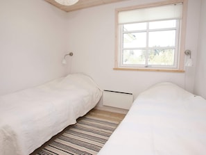 A bedroom with two single beds, a window with blinds, a radiator, and a striped rug. - 5 Star Holiday Home in Brovst (Brovst)