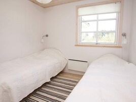 Un dormitorio con dos camas individuales, una ventana con persianas, un radiador y una alfombra a rayas.