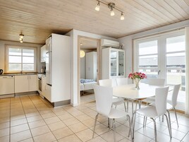 Una cocina moderna con armarios blancos, un comedor con mesa y sillas blancas, y un ventanal con vistas al exterior.