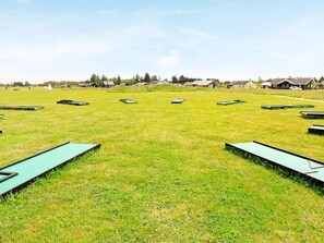 Un campo cubierto de césped con varias estructuras rectangulares verdes, probablemente para deportes o actividades, y casas al fondo.