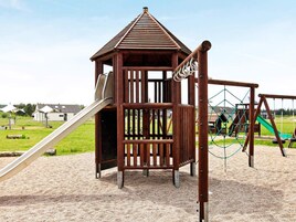 Un parque infantil con una casita de madera, un tobogán y una red de escalada.