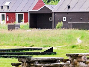 Une grange avec une porte rouge et une porte de garage noire, entourée d’un champ herbeux et d’une structure en bois.