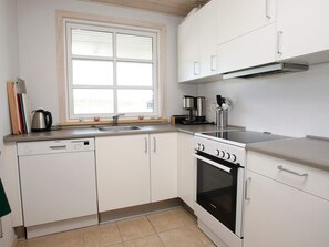 A compact kitchen with a dishwasher, stove, and a window above the sink.