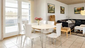 A modern living room with a dining area, featuring a round table, white chairs, a black sofa, and artwork on the walls. - 5 Star Holiday Home in Brovst (Brovst)