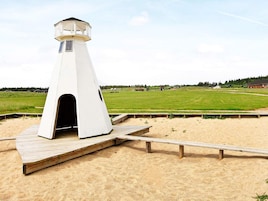 Un faro blanco con una plataforma de madera y una playa arenosa al frente.