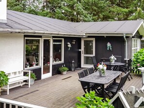 A covered outdoor patio with a wooden deck, a table with chairs, and potted plants.