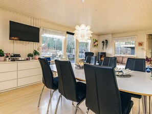 A dining area with a long table, black chairs, a flat-screen TV mounted on the wall, and a fireplace.