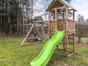 A wooden play structure with a slide and swings in a grassy area.