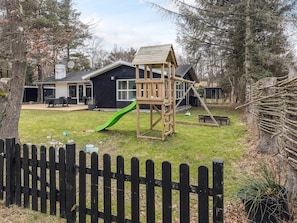 A backyard with a wooden playhouse, a green slide, and a black picket fence.