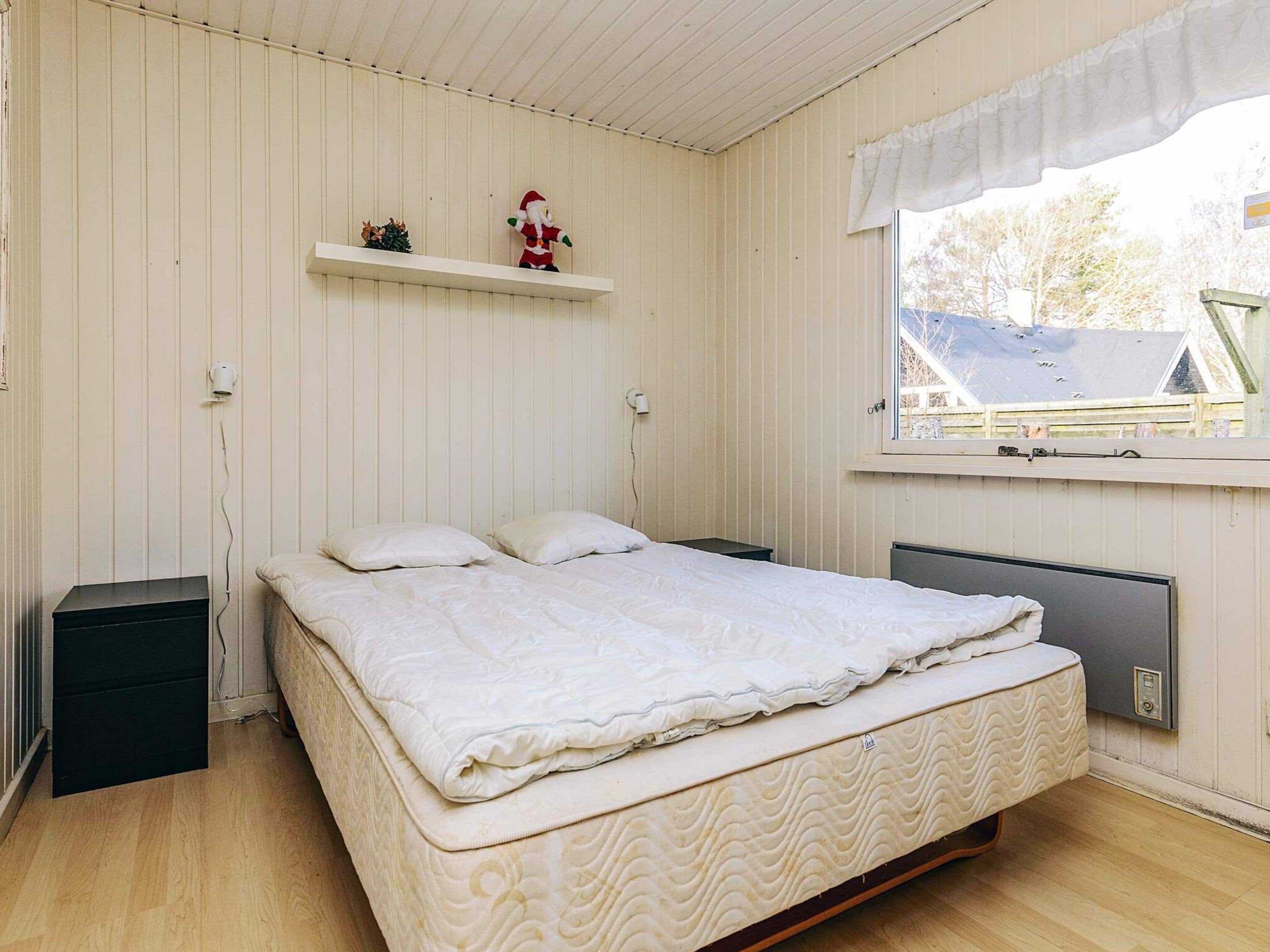 A bedroom with a single bed, a window with a view of the outside, and a shelf with a small decoration.