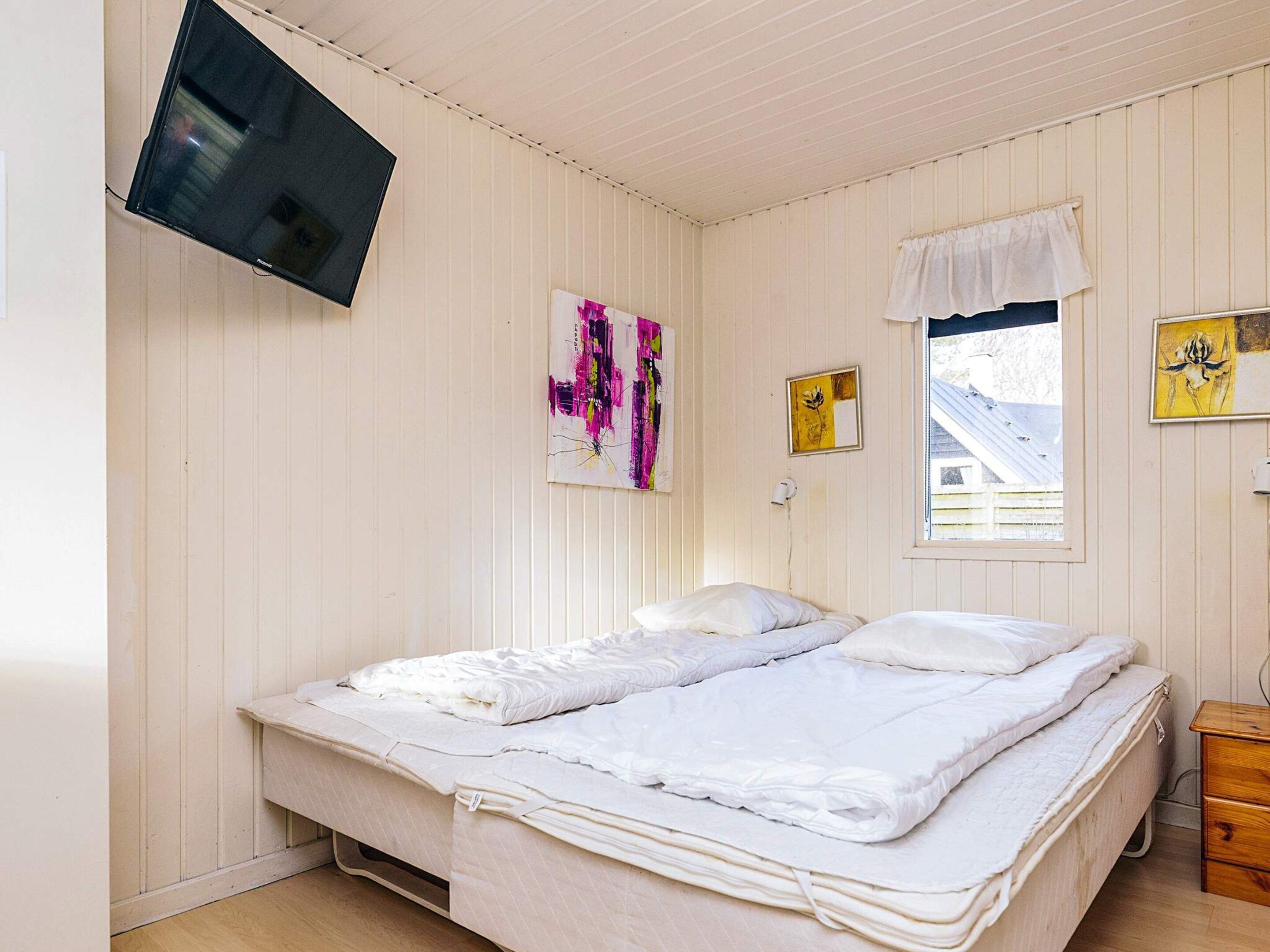 A bedroom with two beds, a TV mounted on the wall, and artwork on the walls.