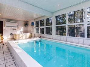 A swimming pool with a view of trees through large windows, a built-in hot tub, and a tiled floor.