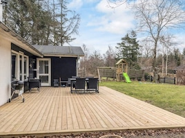 Una terraza de madera con mobiliario exterior, una parrilla de barbacoa y un parque infantil con tobogán.