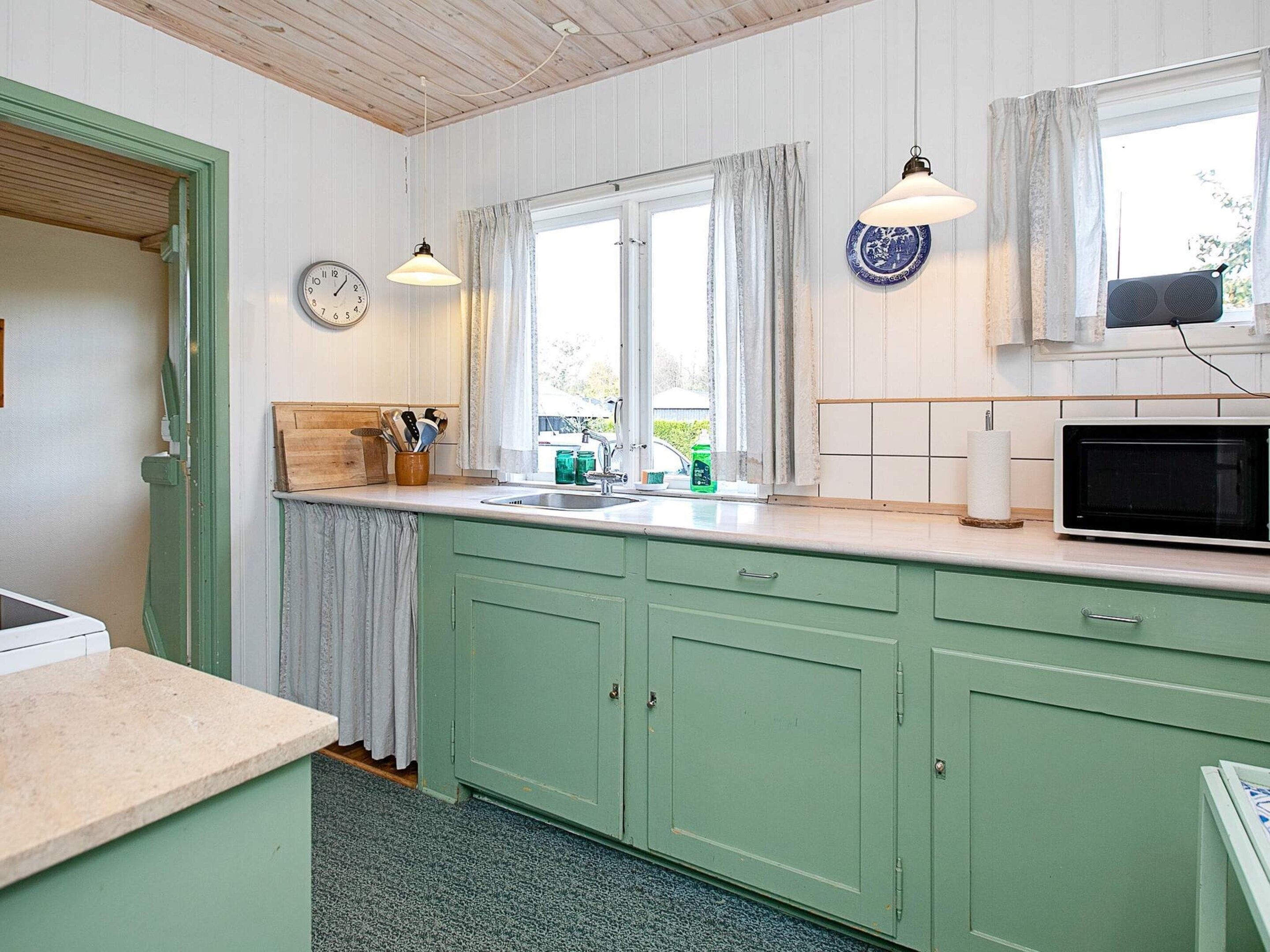 A kitchen with a sink, a microwave, and a clock on the wall.