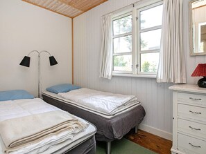 A room with two beds, a window with curtains, a bedside lamp, and a dresser with drawers.
