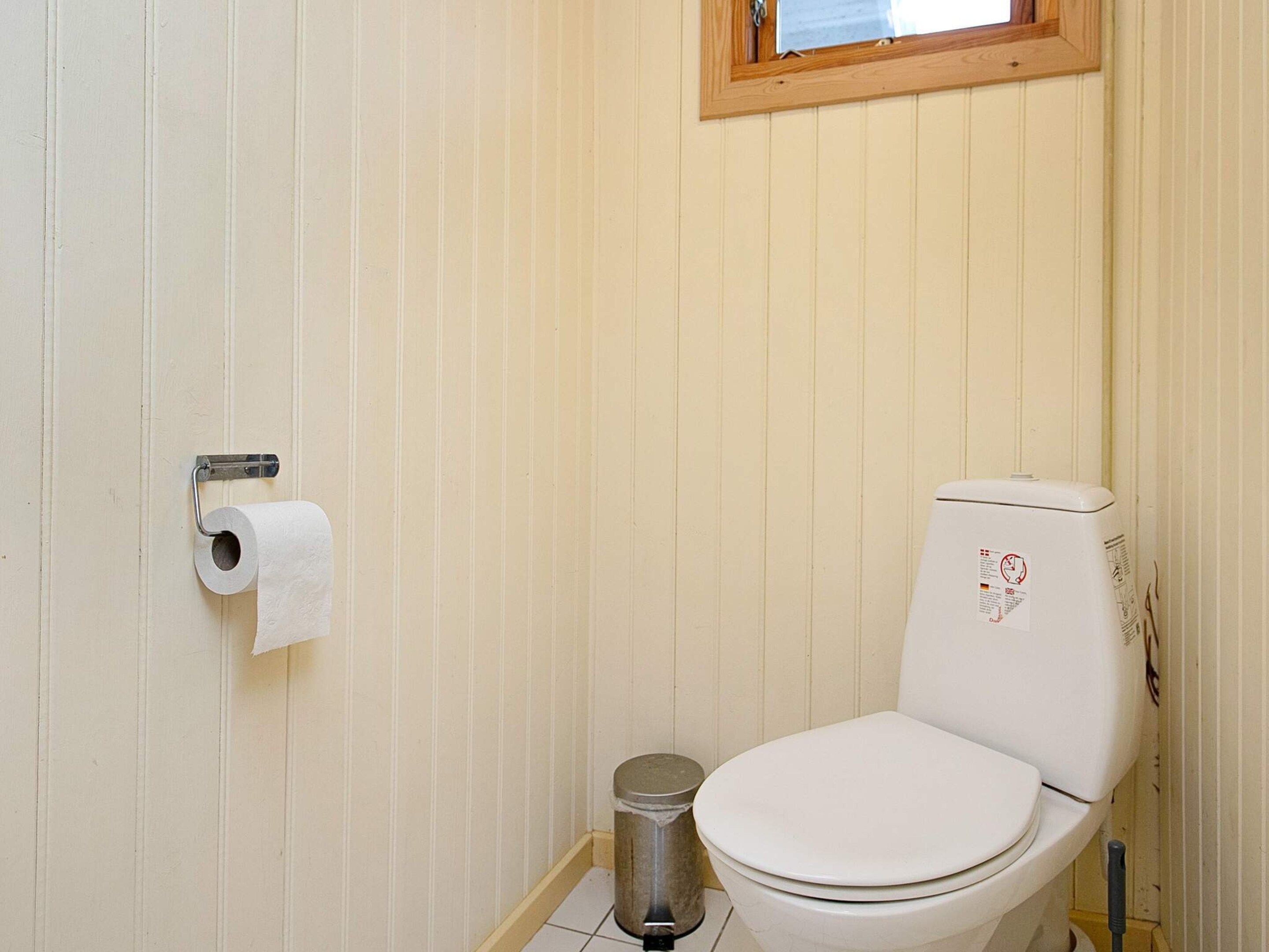 Een kleine, praktische badkamer met een toilet, een prullenbak en een toiletrolhouder aan de muur.