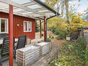 A red wooden building with a covered patio area, outdoor seating, and a garden with trees and plants.