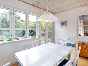 A room with a white table and chairs, large windows, a hanging light fixture, and a wooden cabinet.