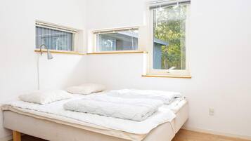A single bed with a headboard, a bedside lamp, and a window with a view of trees.