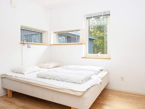 Una cama individual con cabecera, una lámpara de noche y una ventana con vista a árboles.