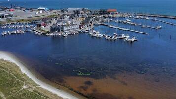 An aerial view of a marina with boats docked, a road leading to the marina, and buildings in the background.