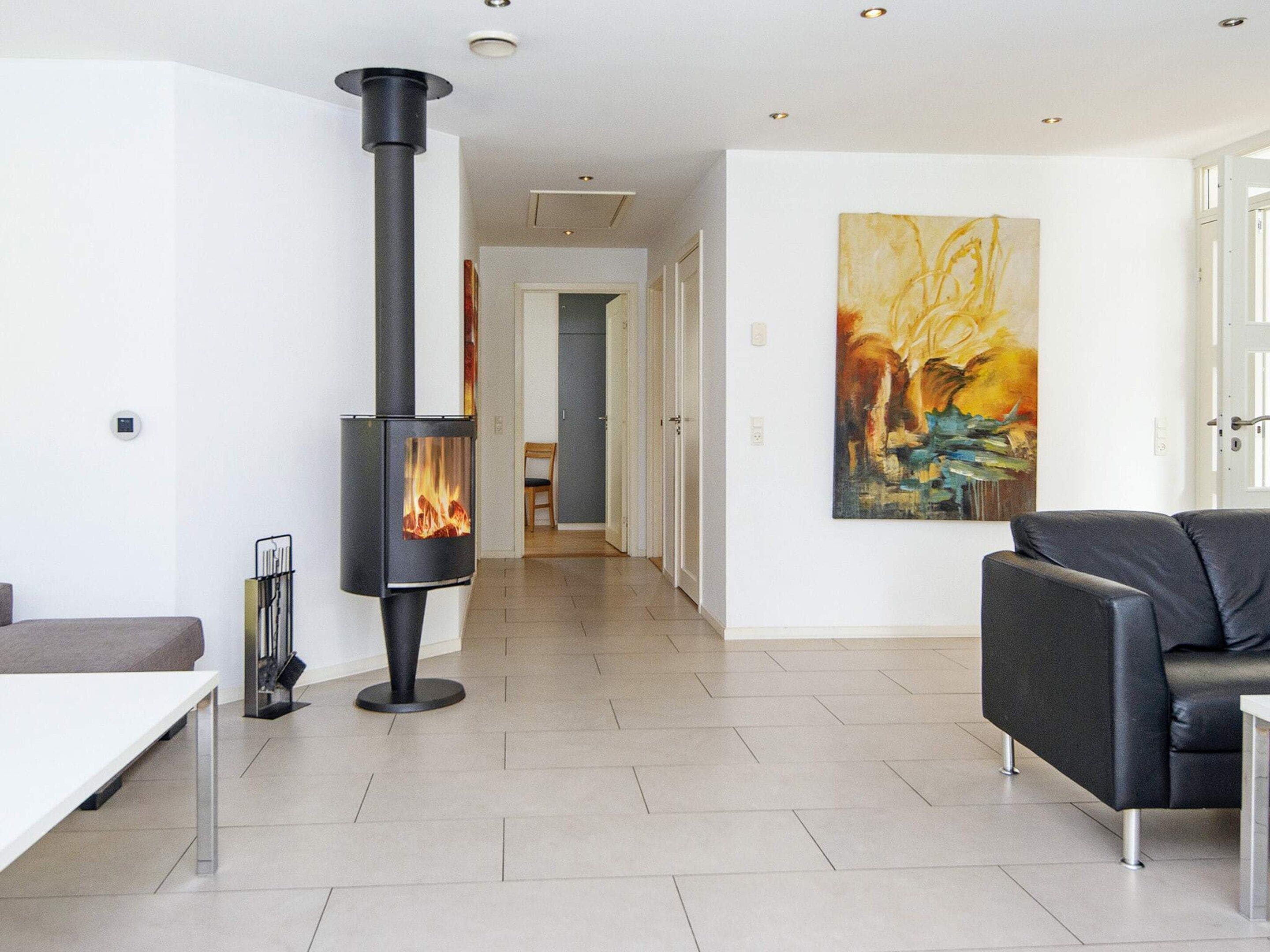 Een moderne woonkamer met een centrale houtkachel, een groot abstract schilderij aan de muur en een bank.