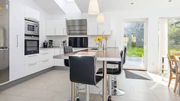 A modern kitchen with stainless steel appliances, a dining area with a large table and chairs, and a view of a garden through a glass door.