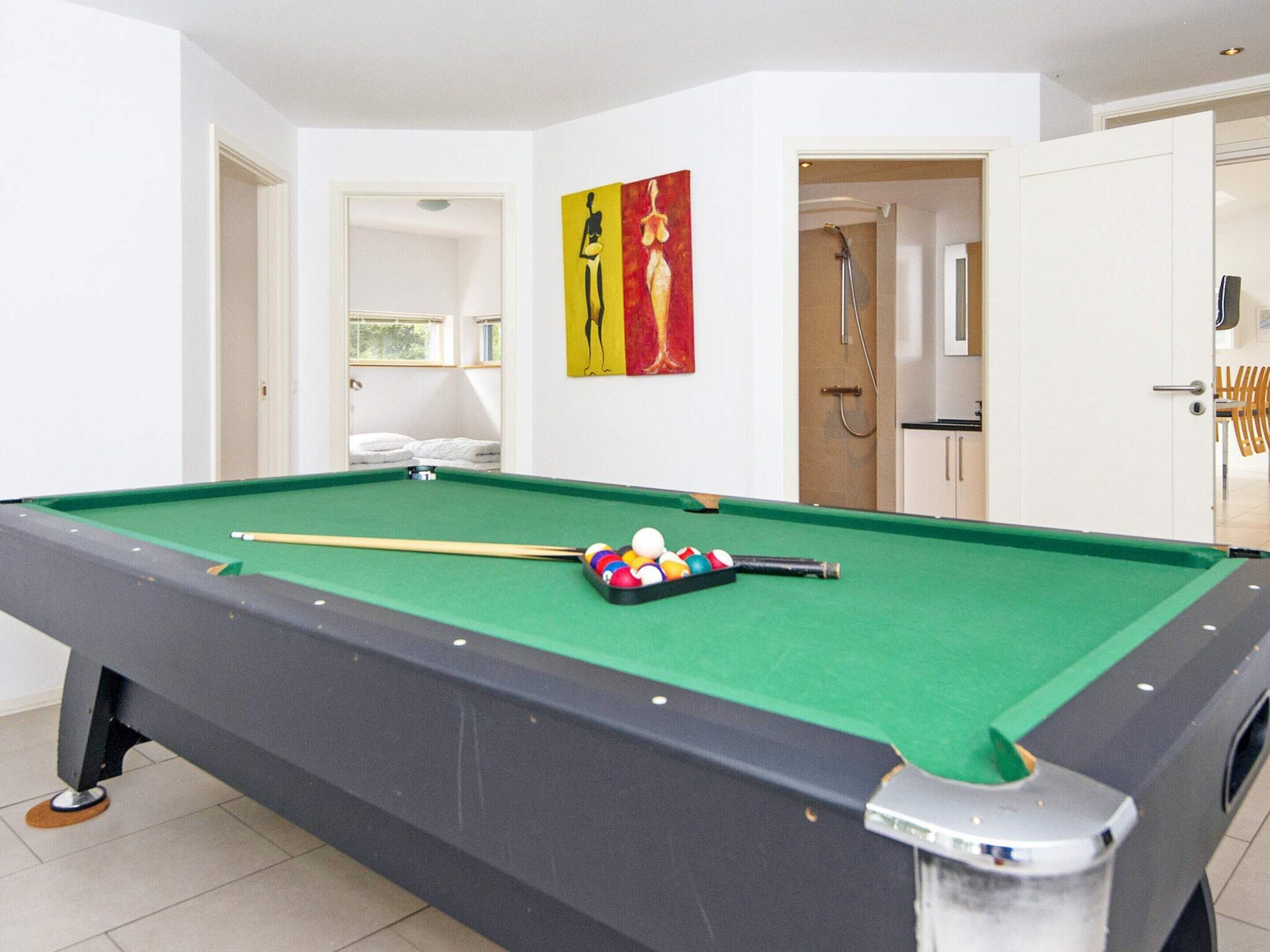 A pool table with balls and a cue stick, a door leading to a bathroom, and a painting on the wall.