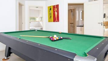 A pool table with balls and a cue stick, a door leading to a bathroom, and a painting on the wall.