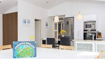 A modern kitchen with a dining table, chairs, a refrigerator, an oven, and a vase with flowers.