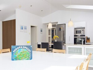 A modern kitchen with a dining table, chairs, a refrigerator, an oven, and a vase with flowers. - 5 Star Holiday Home in Grenaa (Grenaa)