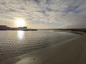 Una orilla tranquila con barcos amarrados, una playa arenosa y cielo despejado.