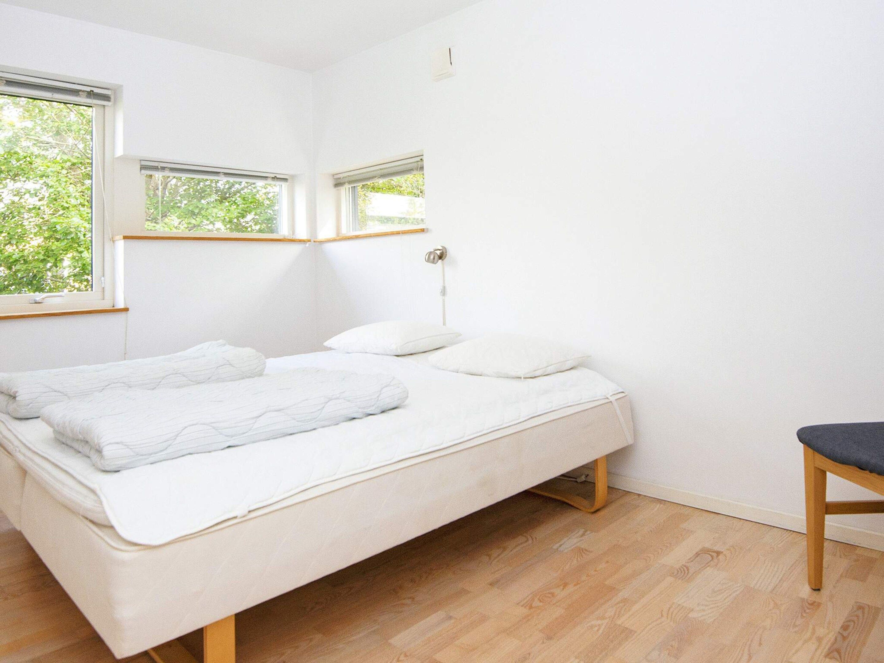 A minimalist bedroom with a single bed, a bedside table, and a chair.