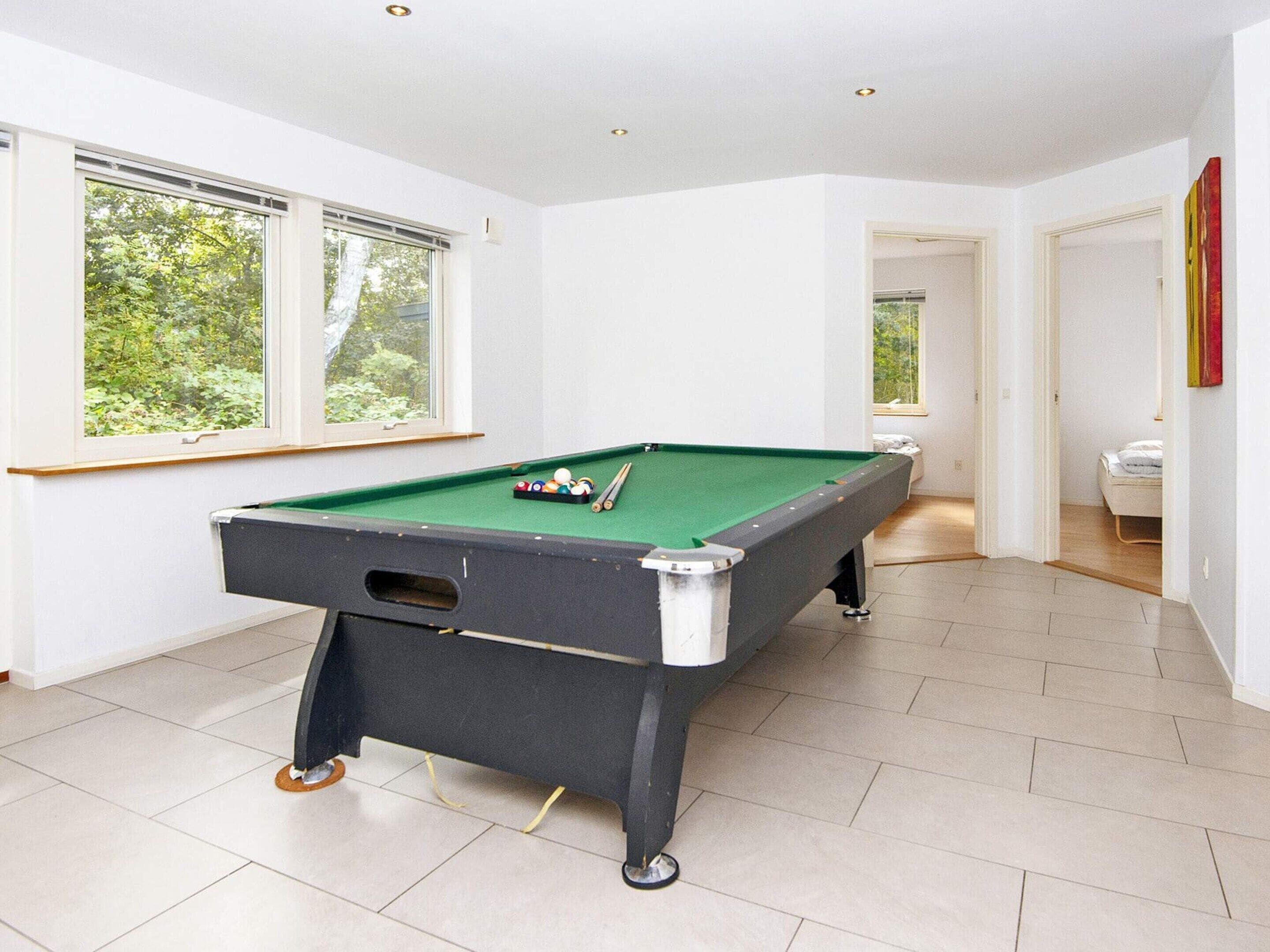 A pool table in a room with white walls and large windows.