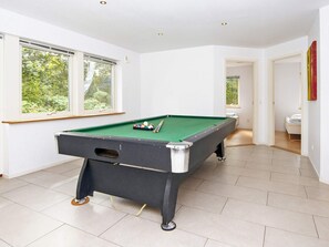 Una mesa de billar en una habitación con paredes blancas y ventanas amplias.